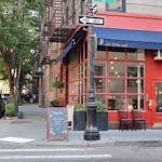 Cozy corner cafe and city street scene in New York with vibrant red facade and sidewalk seating.