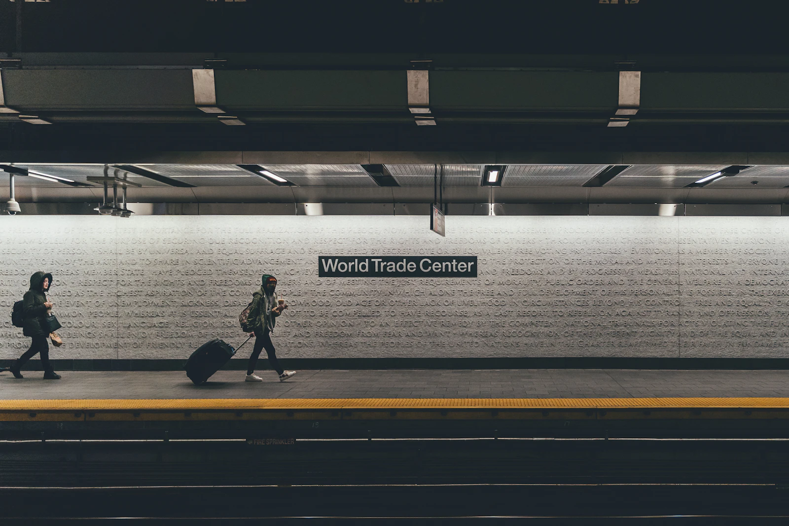 A traveler with a rolling suitcase walking along a subway platform
