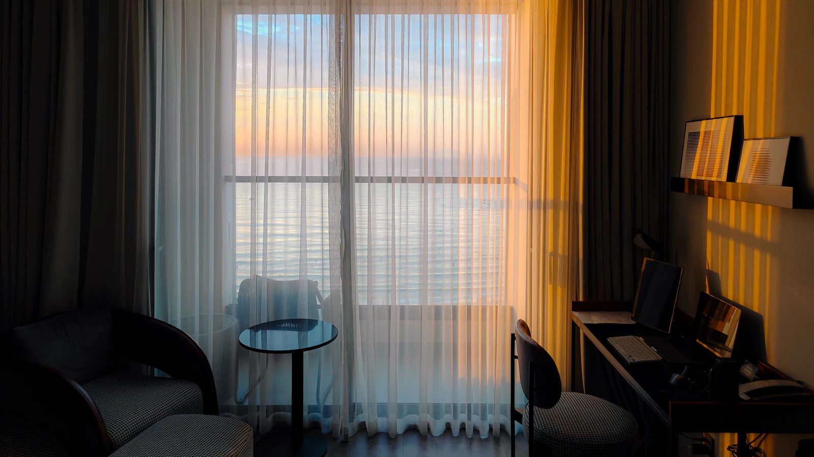A hotel room with golden sunset light glowing through sheer curtains and a view of the sky