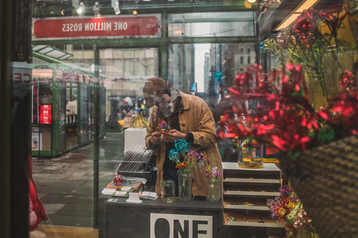 Vendor arranging red flowers inside a glass-fronted holiday kiosk at a Bryant Park holiday market