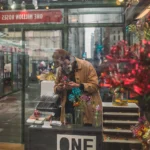 Vendor arranging red flowers inside a glass-fronted holiday kiosk at a Bryant Park holiday market