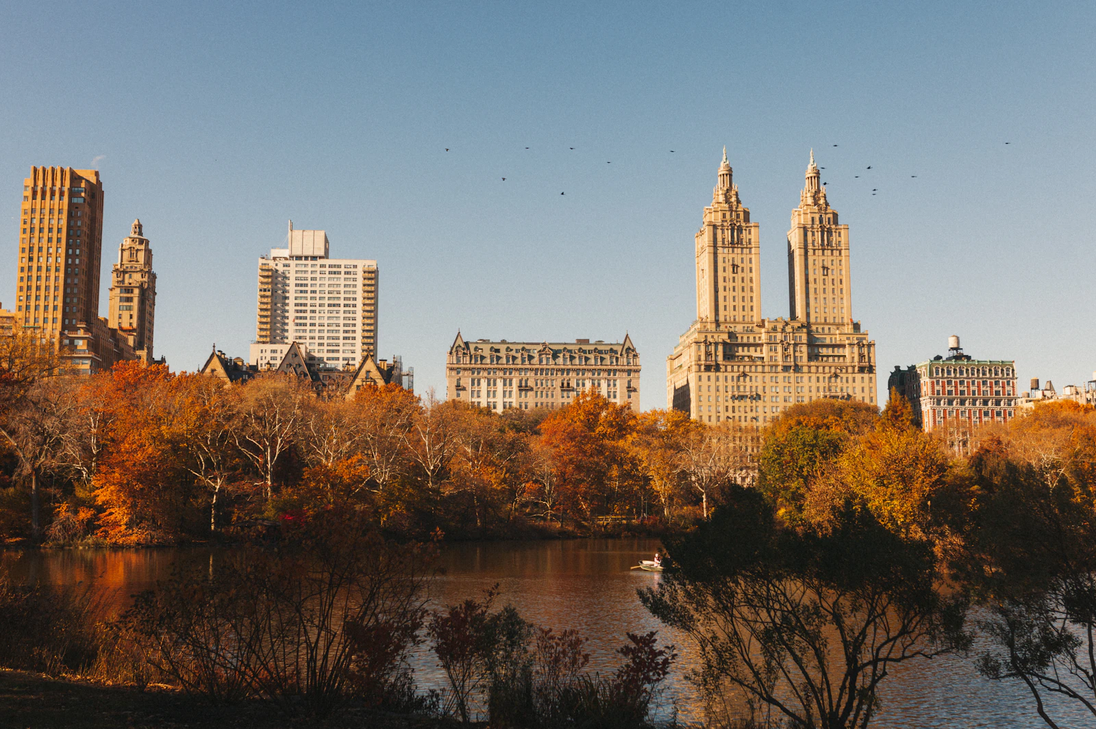 Autumn trees and the twin towers of the Upper West Side skyline reflected in a Central Park pond