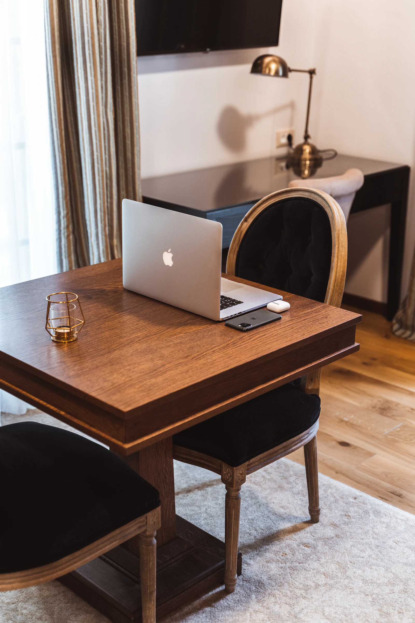 A silver laptop on a wooden table with a small candle holder and a phone beside it