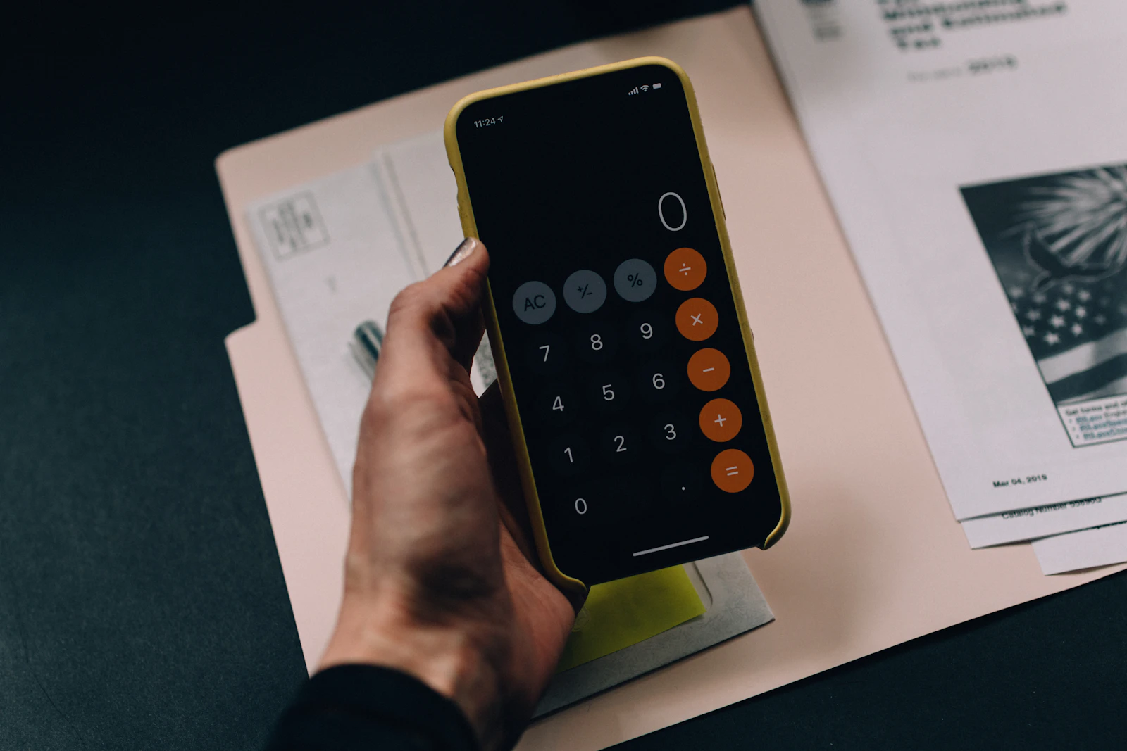 A hand holding a smartphone showing a calculator app over a paper folder
