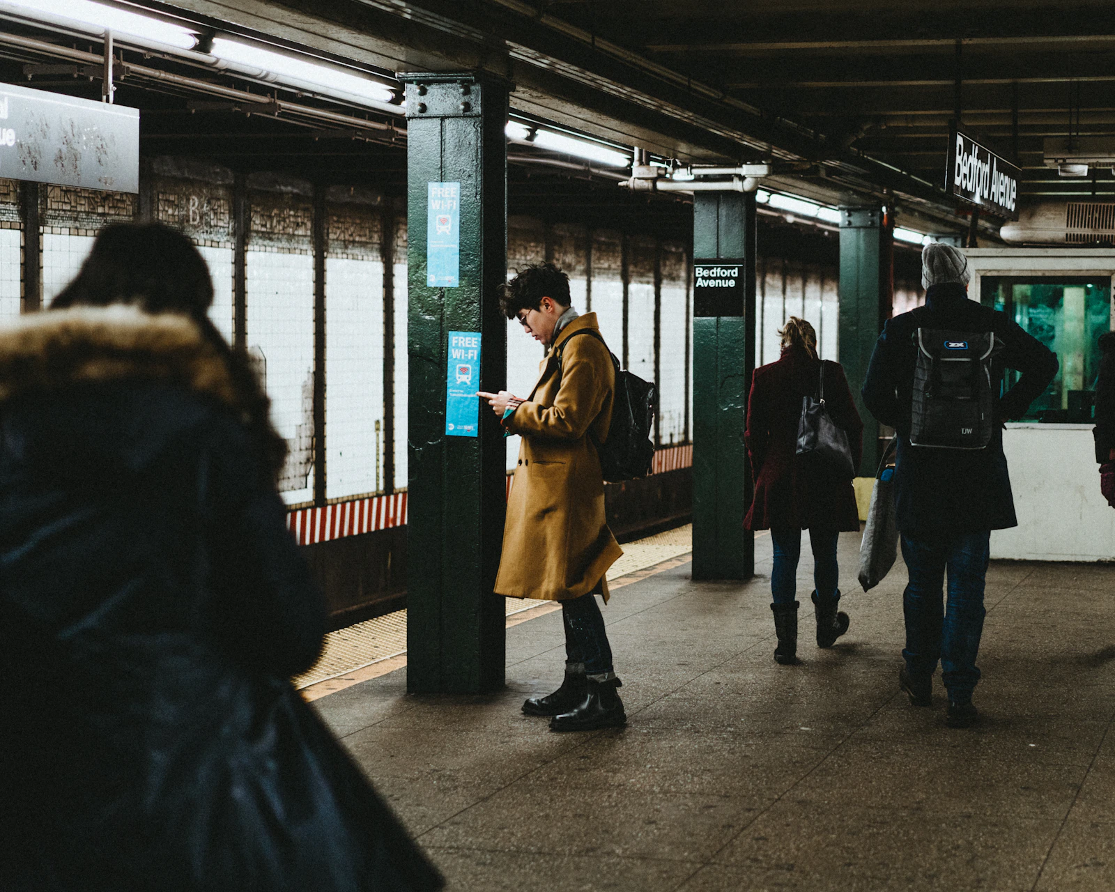 A man in a tan coat checking his phone on a subway platform