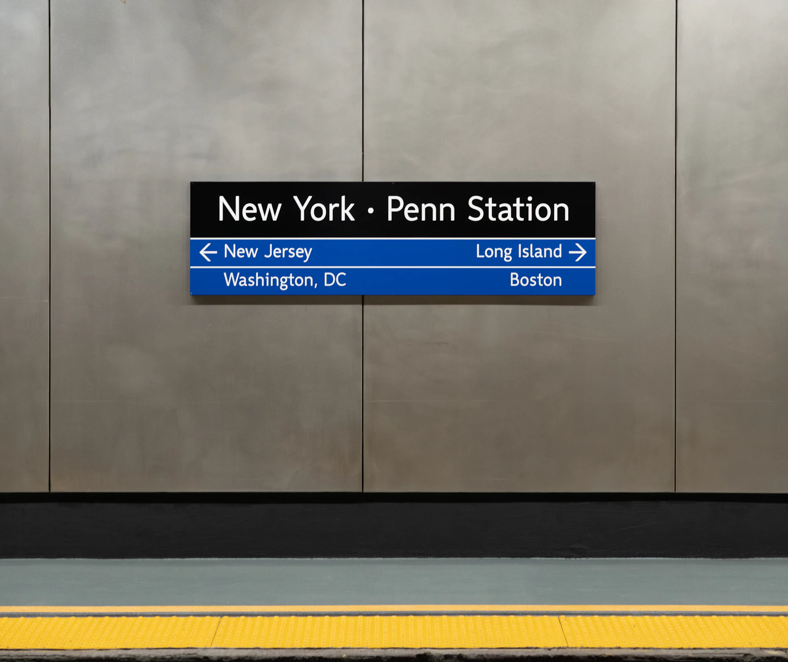A blue sign at New York Penn Station pointing to New Jersey, Long Island, Washington and Boston platforms