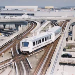 A white automated train on elevated guideways beside airport terminal roads