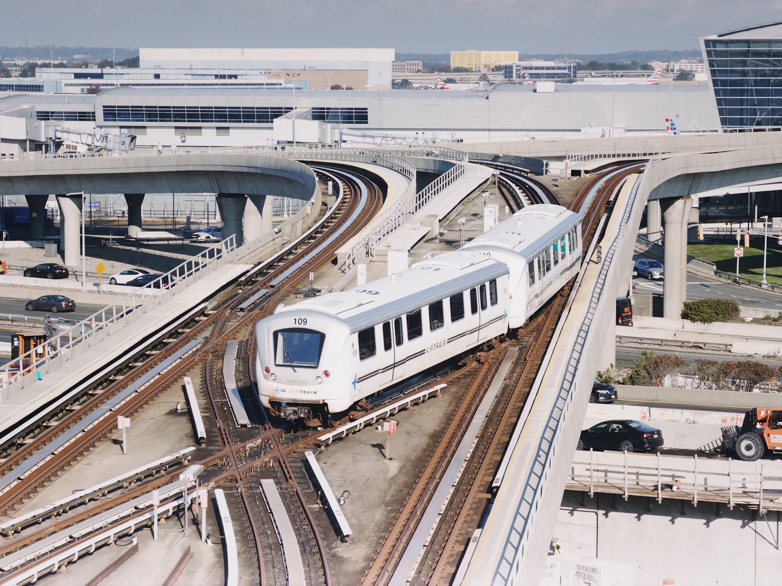 A white automated train on elevated guideways beside airport terminal roads