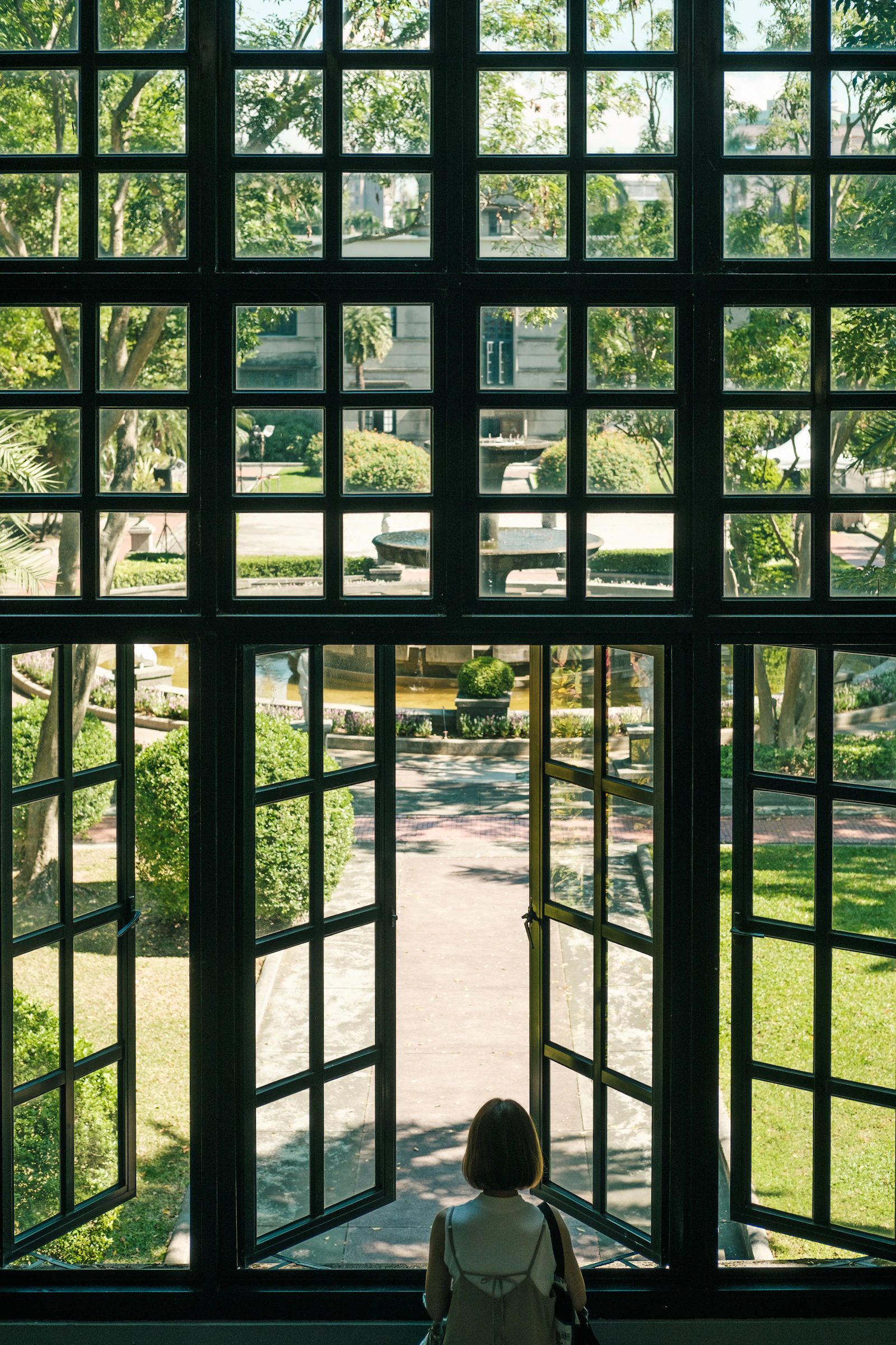 A garden courtyard with a fountain seen through open black steel-framed windows