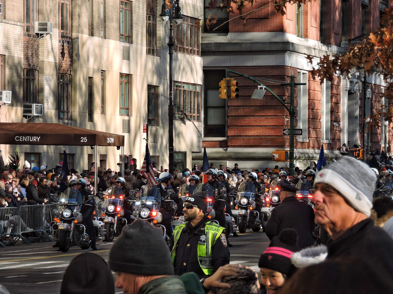 Spectators in winter coats behind barricades as police motorcycles pass on a Manhattan street