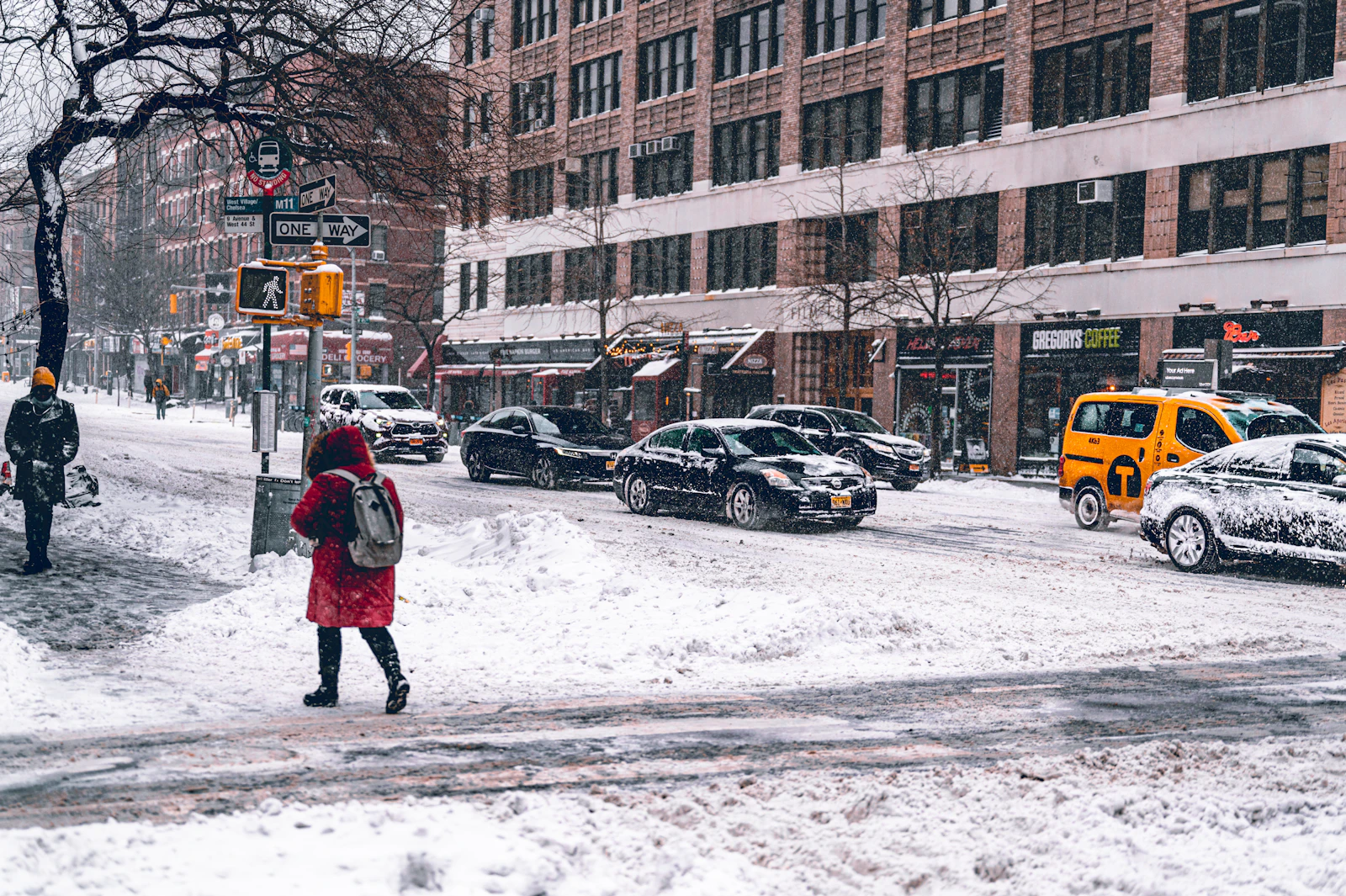 A woman in a red coat crossing a snowy, slushy city street with taxis and cars