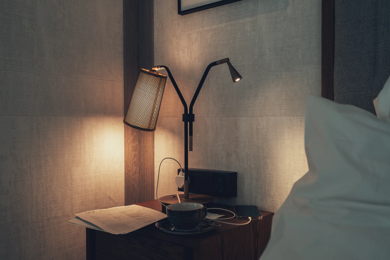 Bedside lamp, loose papers and a coffee cup on a hotel room nightstand
