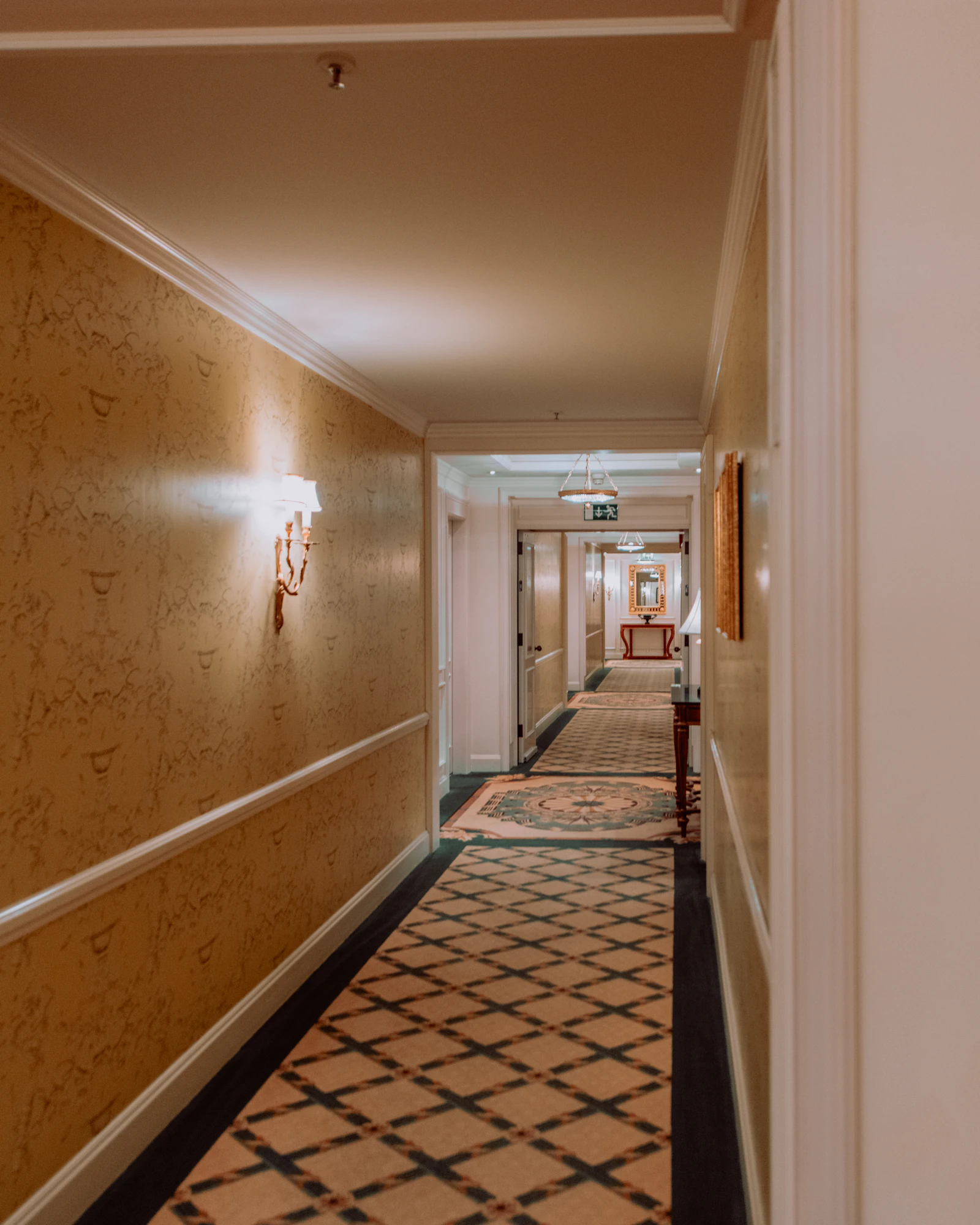 A long carpeted hotel corridor with wall sconces and doors on both sides