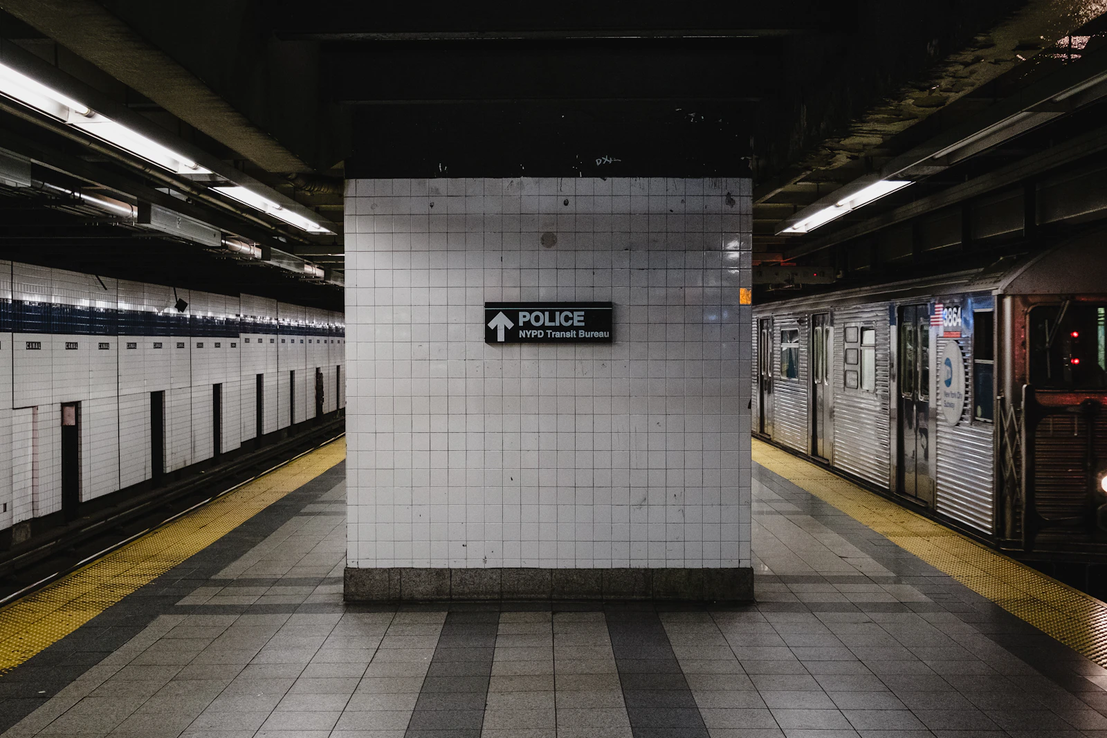 An empty subway platform with a tiled column and a train waiting at the edge