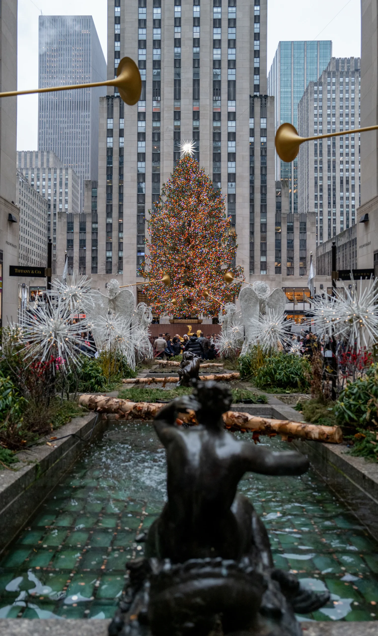 The Rockefeller Center Christmas tree seen from the Channel Gardens, with white angel sculptures along the walkway