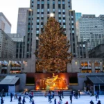 The Rockefeller Center Christmas tree lit above the ice rink and the golden Prometheus statue, with skaters on the ice