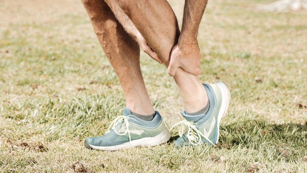 Runner holding a sprained ankle on a city sidewalk after a running injury