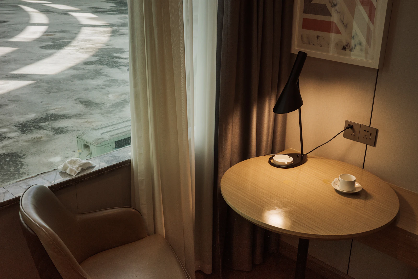 An armchair and a round table with a lamp and a cup beside a curtained window