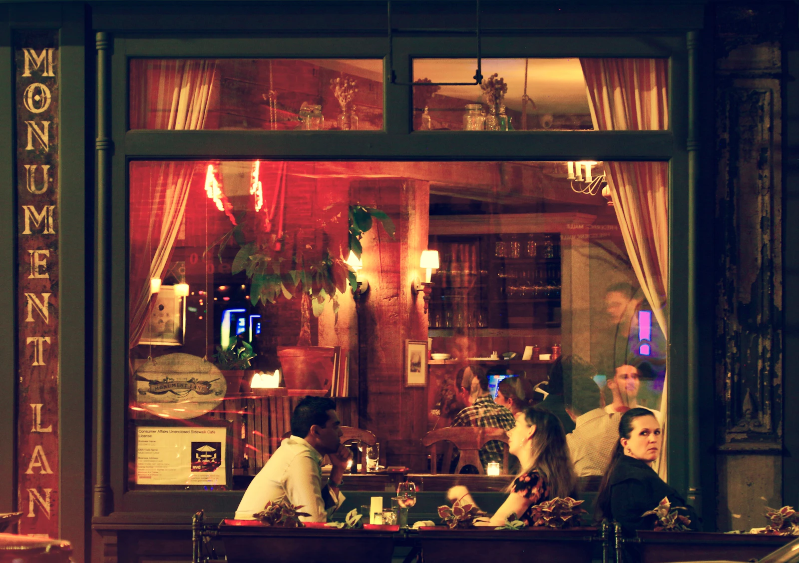 A warmly lit restaurant window at night with diners seated inside