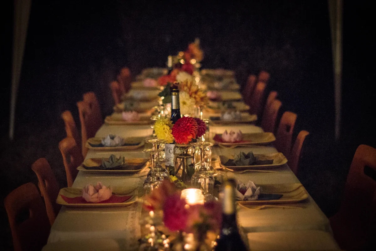 A long dining table set for dinner with flowers and glowing candles in a dim room