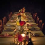 A long dining table set for dinner with flowers and glowing candles in a dim room