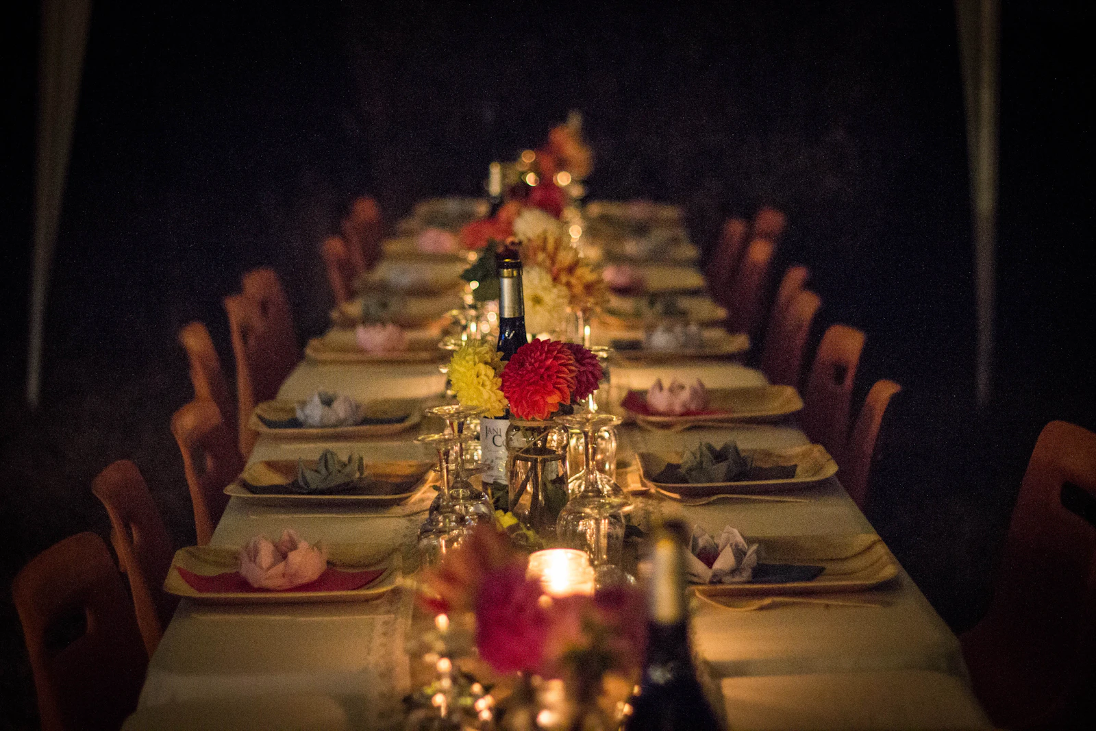 A long dining table set for dinner with flowers and glowing candles in a dim room