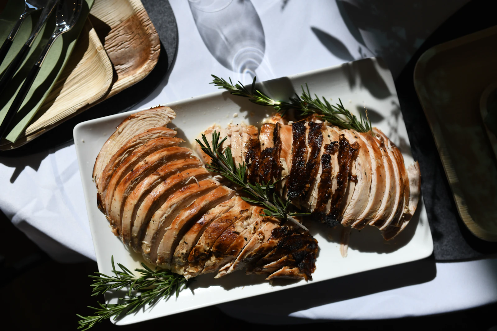Sliced roast turkey with rosemary on a white rectangular platter