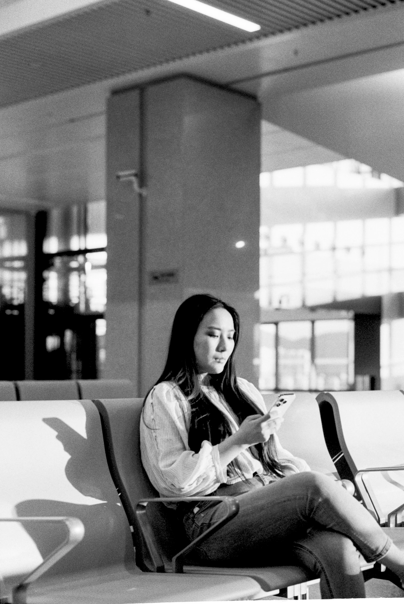 A woman looking at her smartphone while seated in a bright terminal