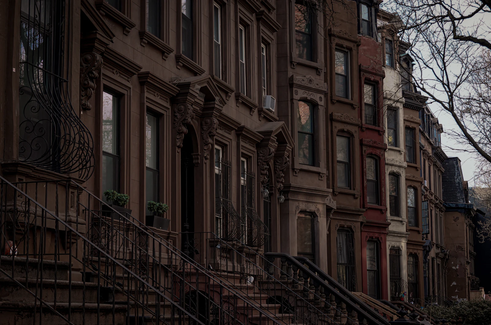 A row of brownstone townhouses with iron railings and stoops in dim evening light