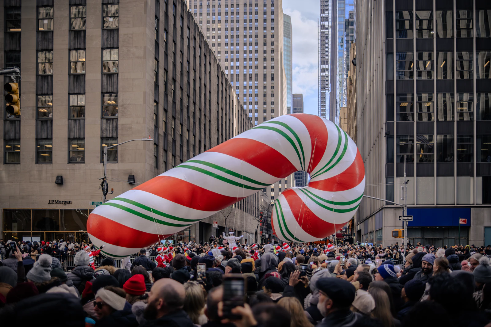 Giant candy cane balloon floating above spectators on a Midtown street during a Thanksgiving parade
